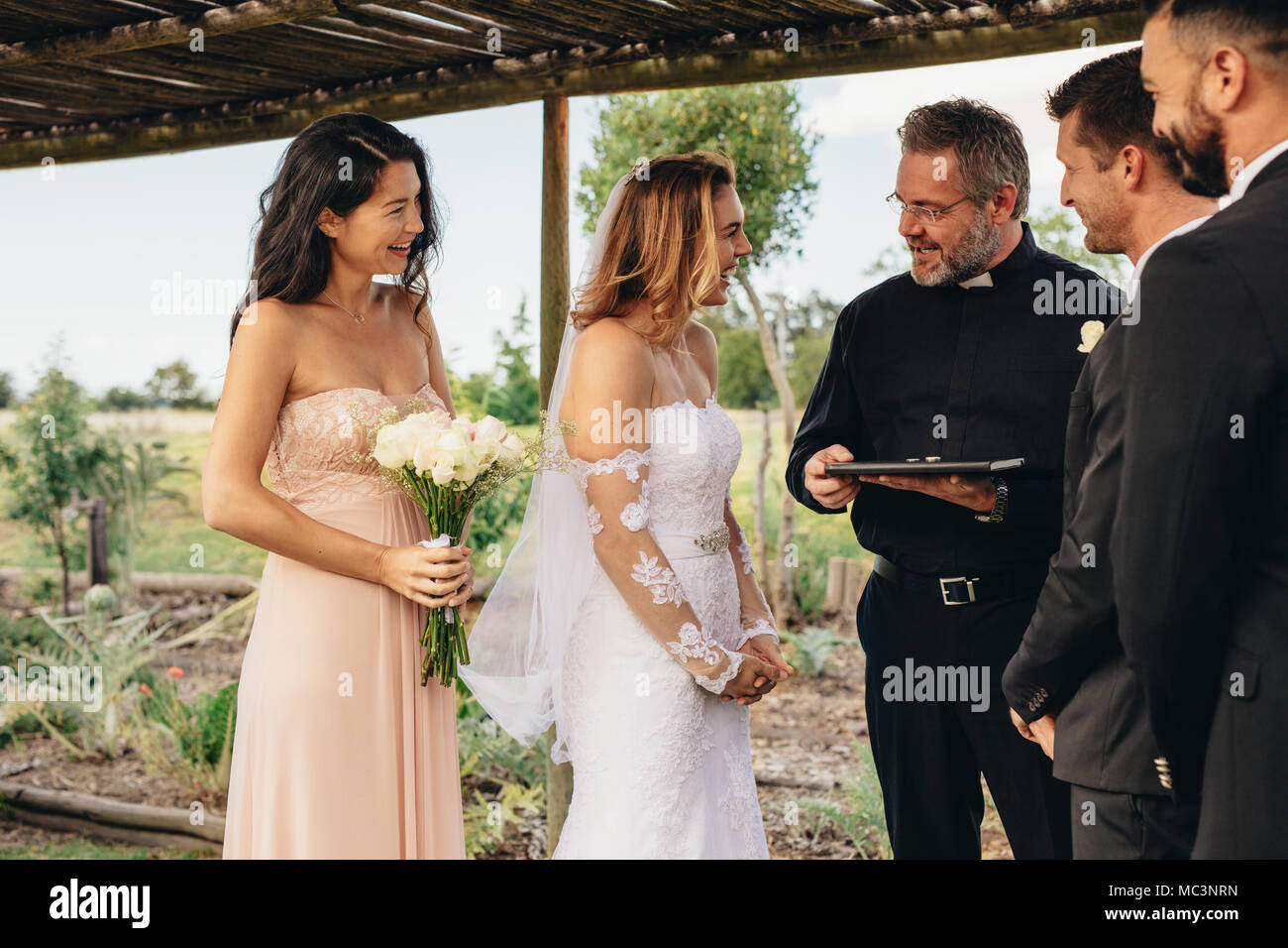 Smiling bride parlant avec prêtre après la cérémonie de mariage mariage en vertu de l'arch. Belle cérémonie de mariage en plein air. Banque D'Images Smiling bride parlant avec prêtre après la cérémonie de mariage mariage en vertu de l'arch. Belle cérémonie de mariage en plein air. Banque D'Images