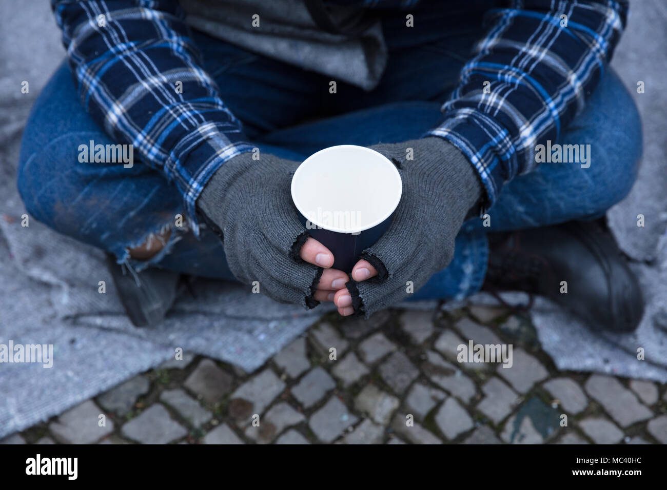 La main de mendiant portant des gants Holding Disposable Cup Banque D'Images