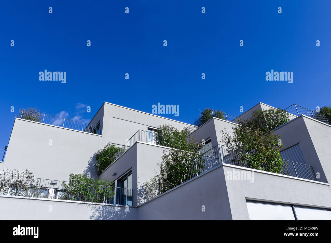 Immeuble gris avec une architecture moderne et un grand balcon avec des plantes vertes. Derrière un fond bleu du ciel. Vue de dessous. Banque D'Images