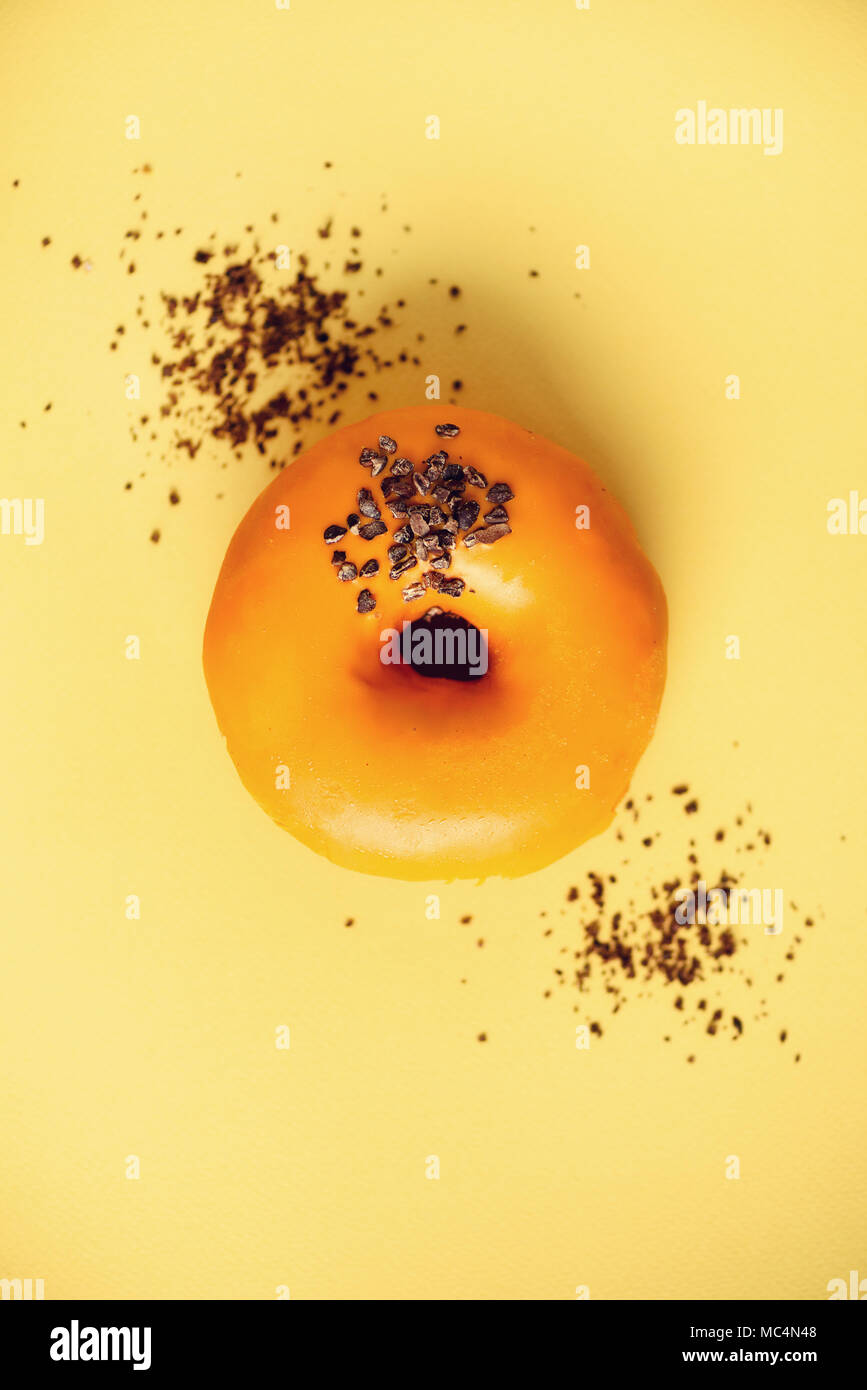 Sweet donut glaçage à l'orange et de chocolat sur fond gris. Beignet savoureux sur la texture jaune pastel, copy space, vue du dessus Banque D'Images