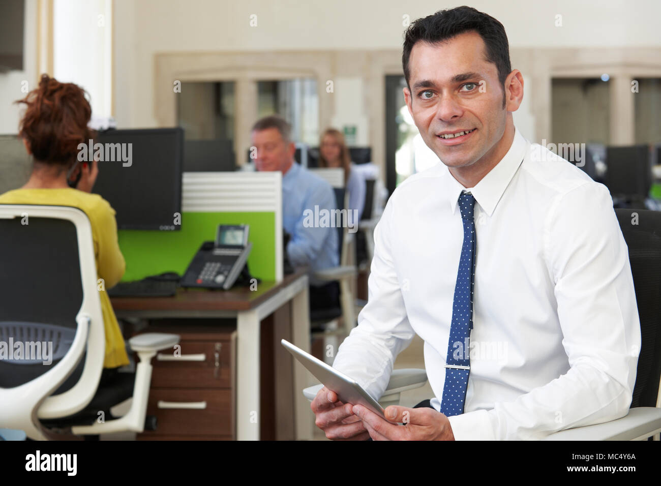 Portrait Of Businessman With Digital Tablet Sitting in Busy Modern Office Banque D'Images