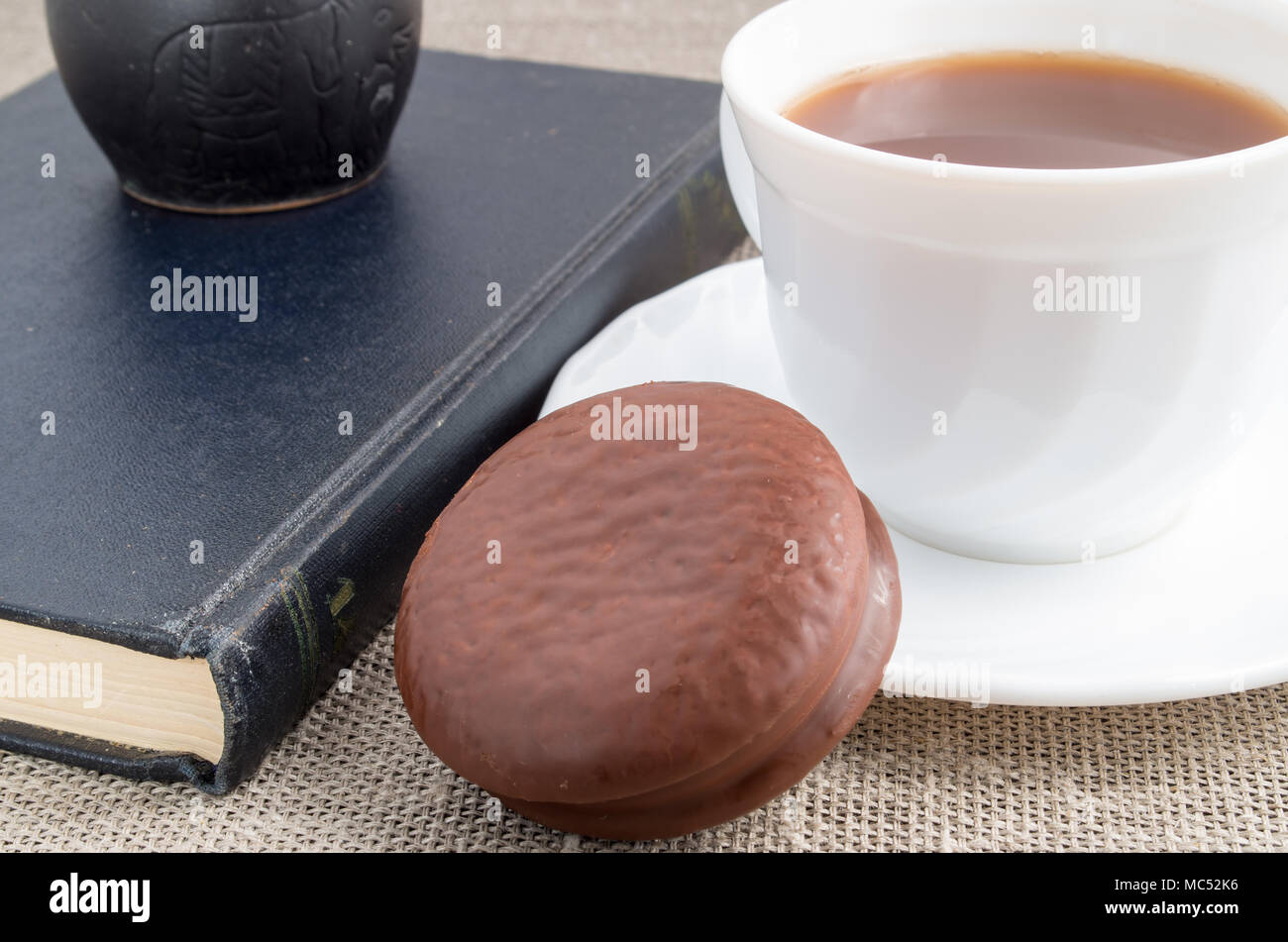 Vue rapprochée sur white cup avec le cacao et le chocolat noir biscuit sur vieux livre sur fond de tissu Banque D'Images