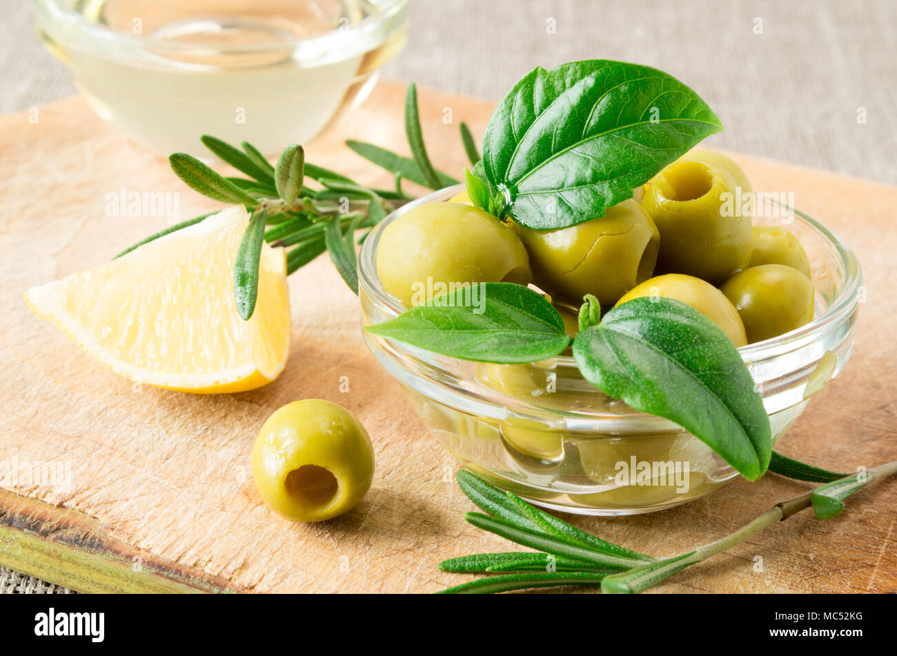 Tasse en verre avec des olives dénoyautées vert décoré d'herbes sur un socle en bois avec une faible profondeur de foyer. Banque D'Images