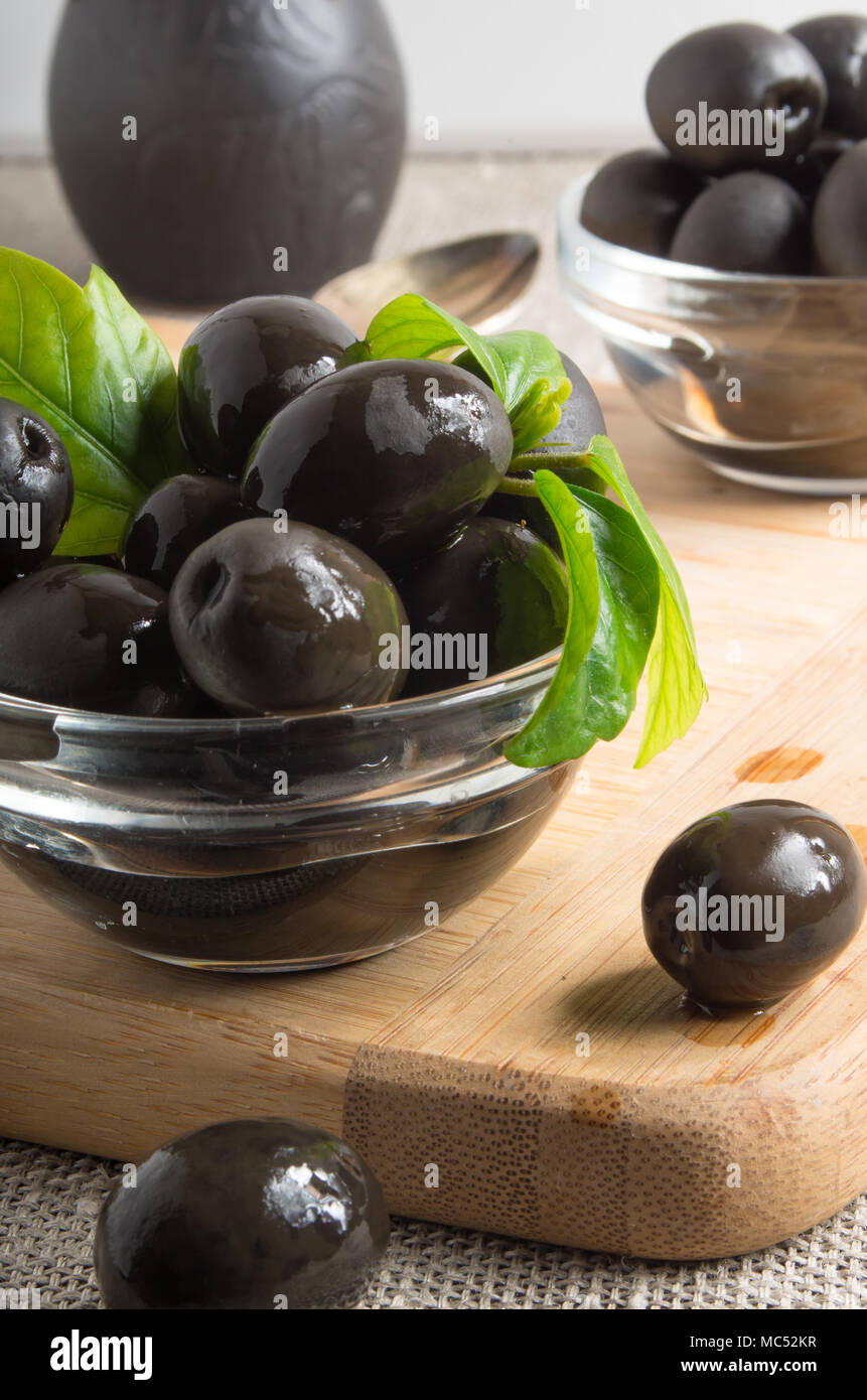 Olives noires dans un bol en verre décoré avec des feuilles vertes sur un vieux tapis de table avec une petite profondeur de champ Banque D'Images