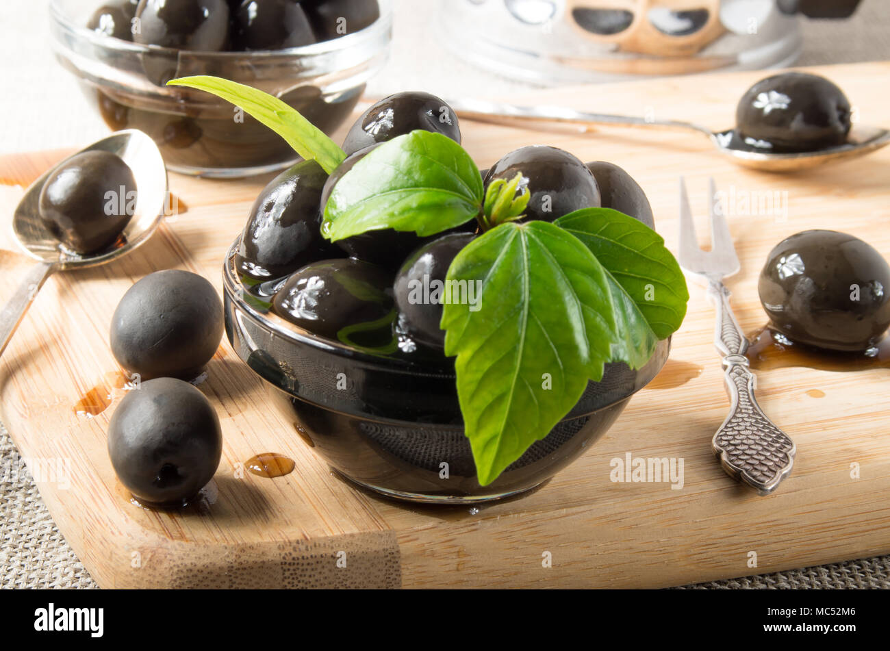 Olives noires sur une table et en verre tasses décorées avec de l'huile avec des feuilles vertes sur un plateau en bois et la vaisselle vintage avec une faible profondeur de foyer Banque D'Images