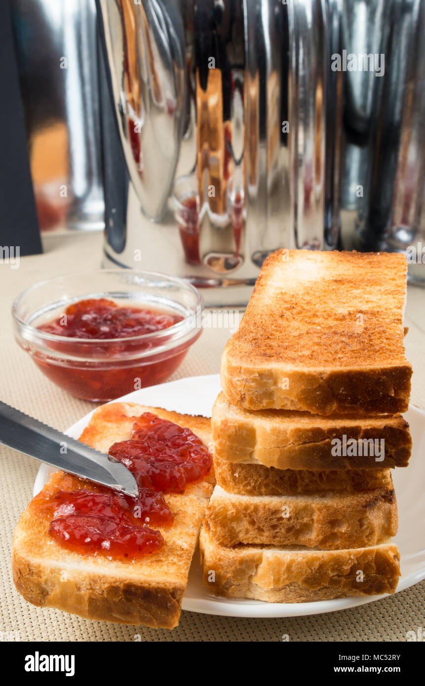 Tranches de pain grillé avec de la confiture de fraise sur la table avec des ustensiles de cuisine avec un arrière-plan flou Banque D'Images