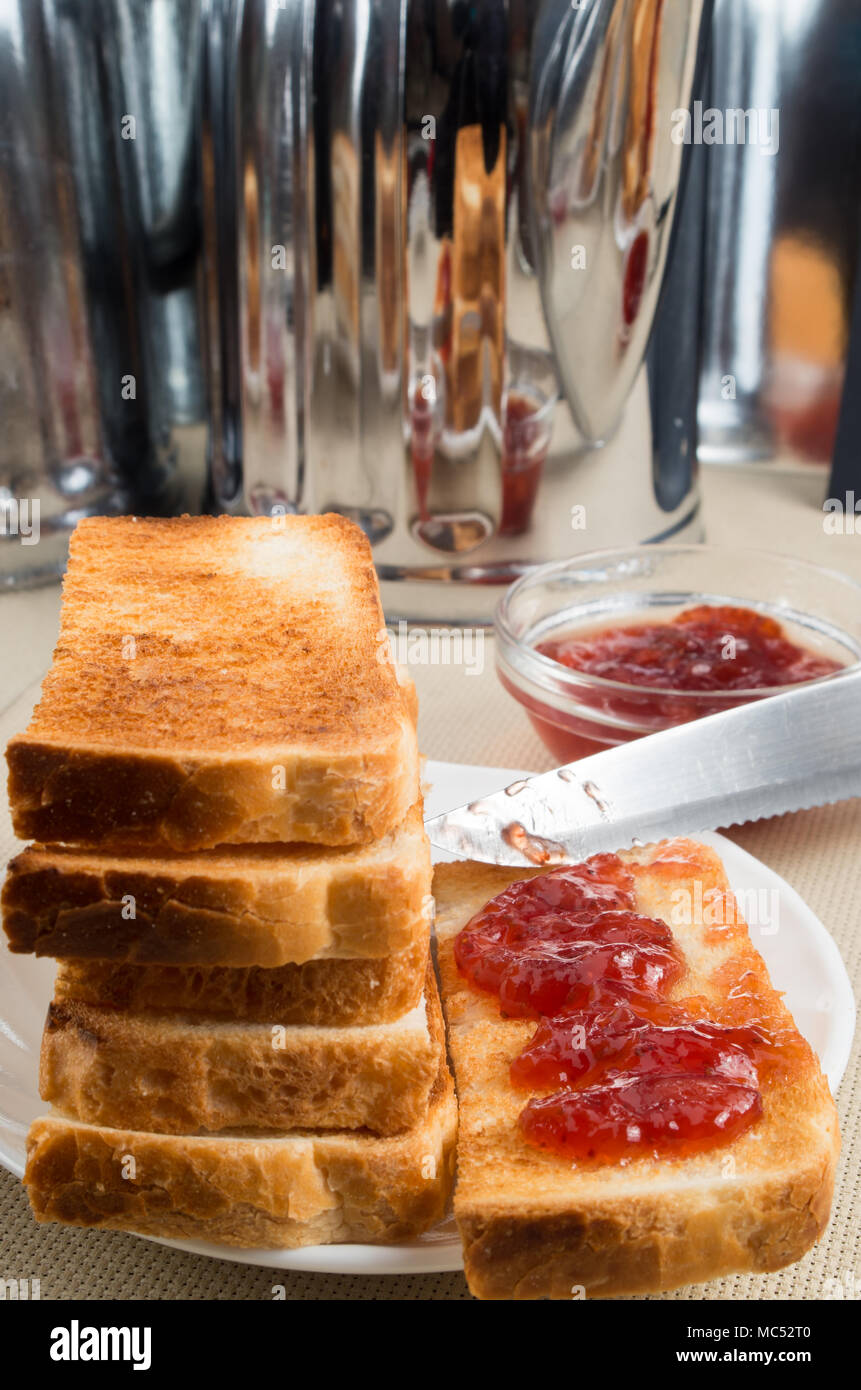 Tranches de pain grillé avec de la confiture de fraise sur la table avec des ustensiles de cuisine avec un arrière-plan flou Banque D'Images