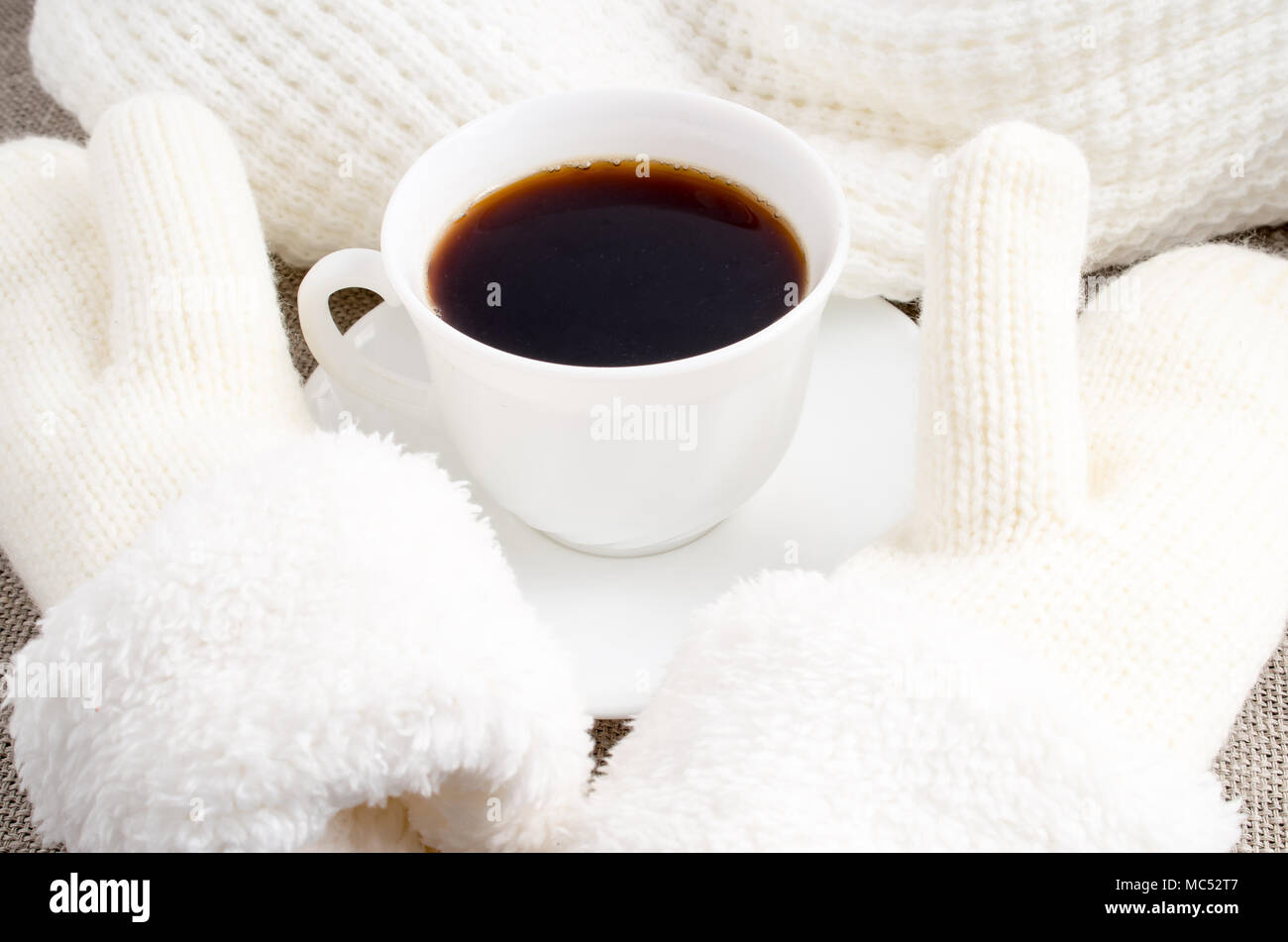 Tasse blanche avec du café chaud à côté du mitaines de laine blanche et un foulard Banque D'Images