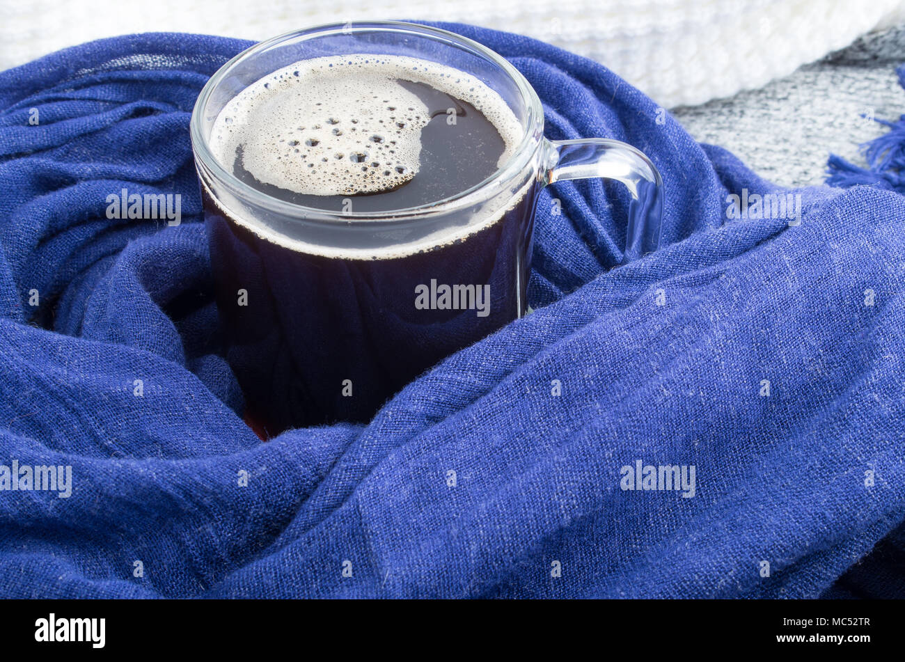 Mug en verre transparent avec café enveloppé dans l'écharpe en coton bleu close-up Banque D'Images