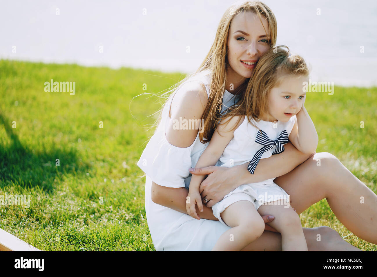 Une jeune et belle maman aux cheveux longs assis dans le parc avec sa belle petite fille Banque D'Images