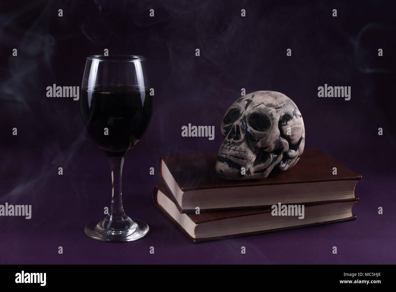 Livres sur le crâne et un verre de vin sur fond violet sombre et fumé, Halloween, concept clé faible Banque D'Images