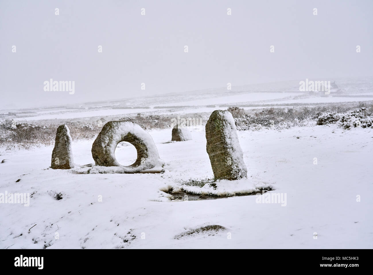 Les hommes d'un Âge de Bronze Tol stones pendant la neige le 18 mars 2018 avec la ferme abandonnée maison dans l'arrière-plan. National Trust/ Angleterre Historique Banque D'Images