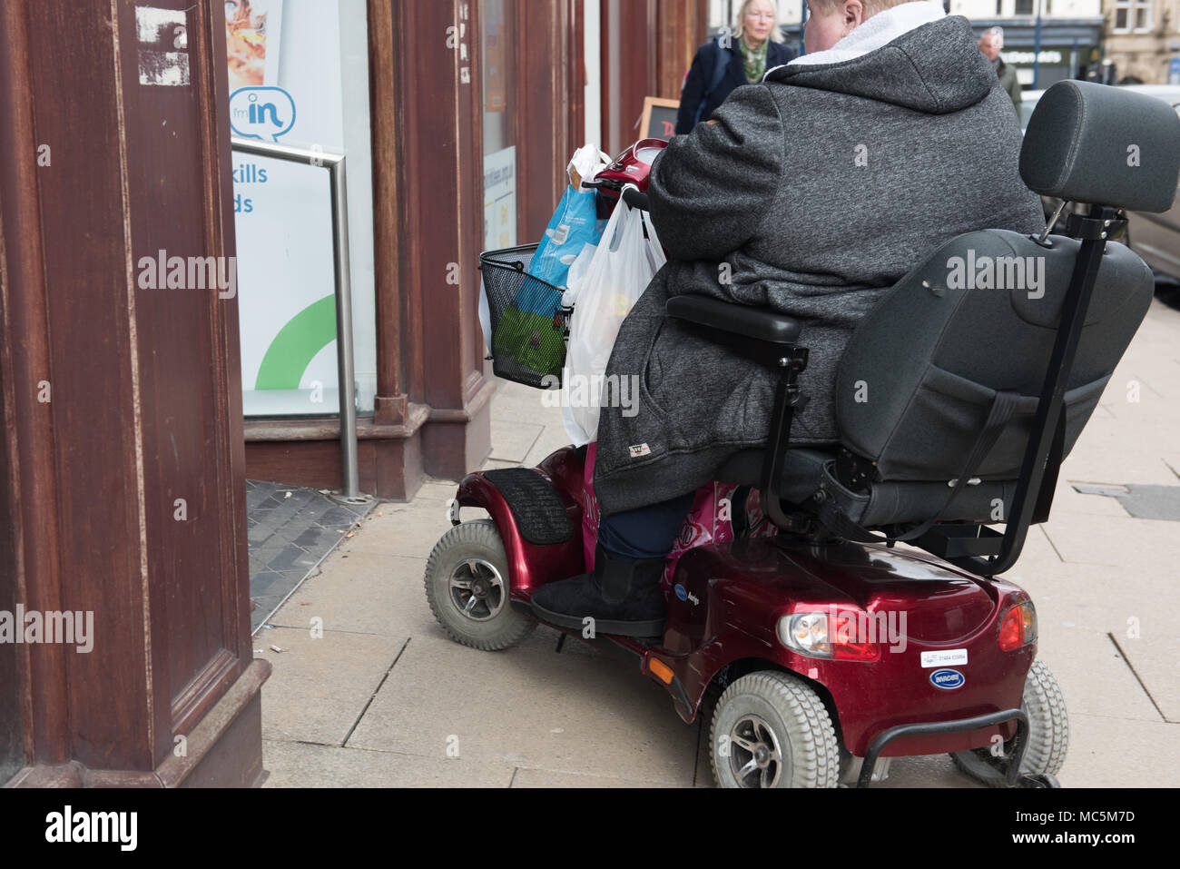 Un individu utilisant un scooter de mobilité sur un trottoir de ville occupé — accessibilité et indépendance dans un environnement urbain Banque D'Images