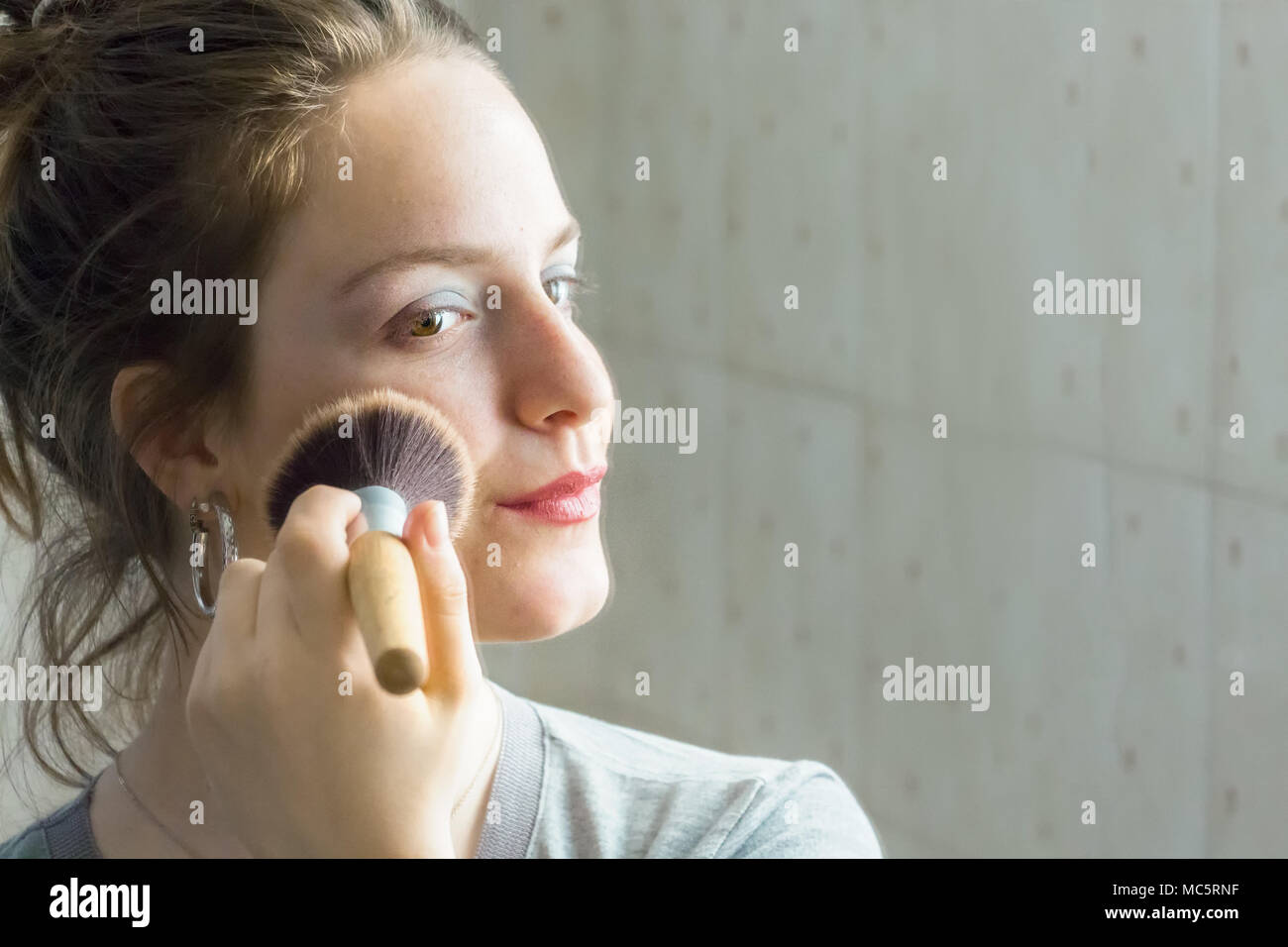 Adolescentes l'application de poudre avec une brosse à son reflet dans un miroir à la maison. Banque D'Images