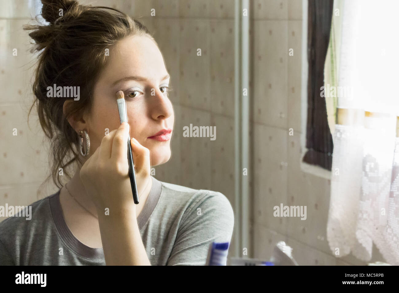 L'application de l'ombre à paupières adolescentes à son reflet sur un miroir à la maison. Banque D'Images