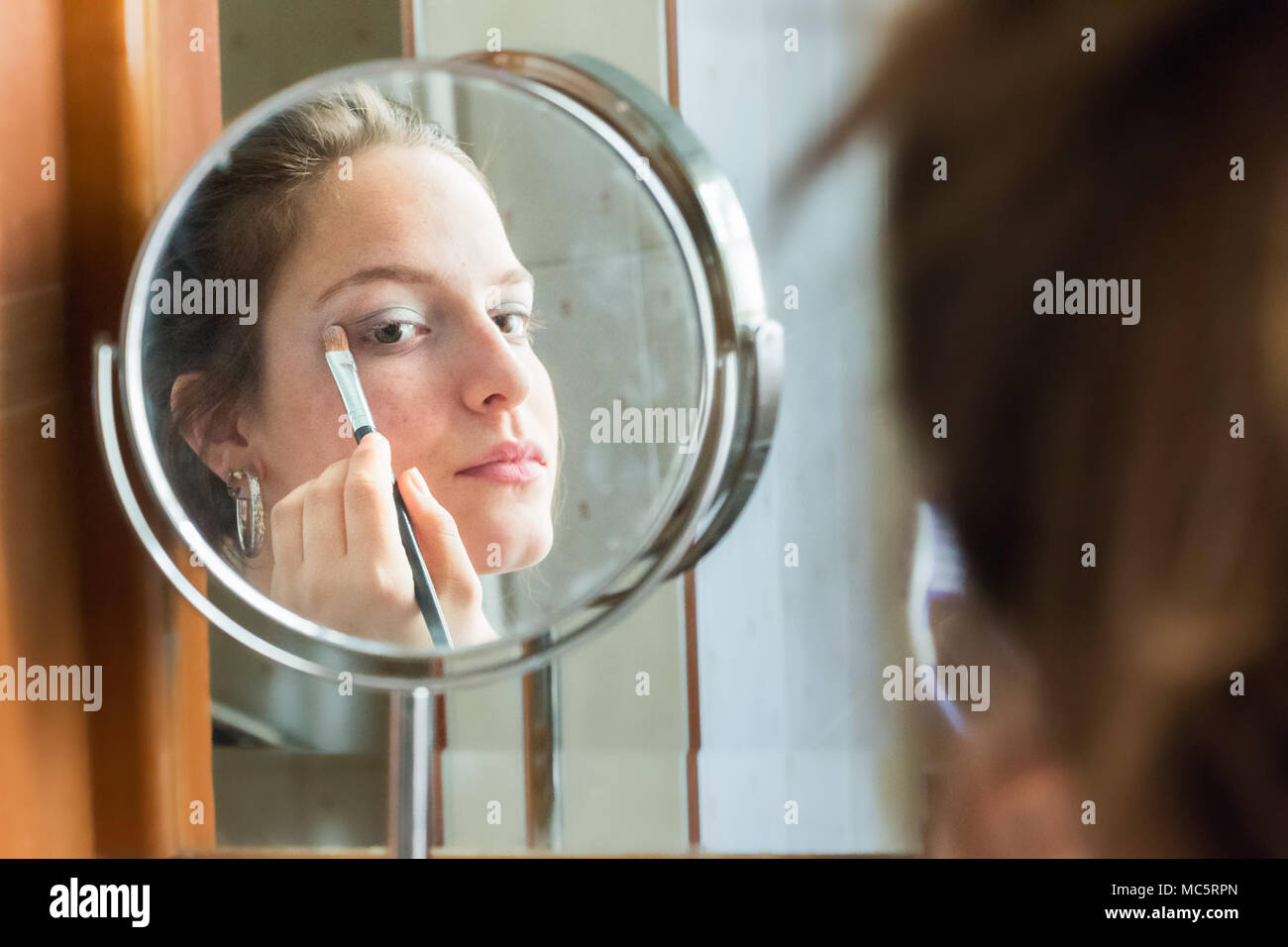 L'application de l'ombre à paupières adolescentes à son reflet sur un miroir rond à la maison Banque D'Images