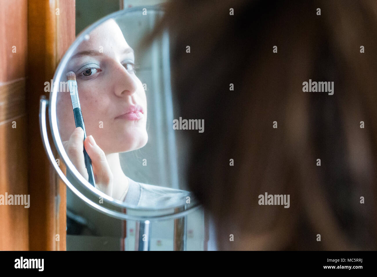 L'application de l'ombre à paupières adolescentes à son reflet sur un miroir rond à la maison Banque D'Images