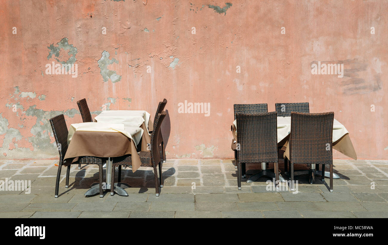 Deux tables de restaurant avec chaises et nappe contre un mur fissuré et délabré sur un soleil brillant Banque D'Images