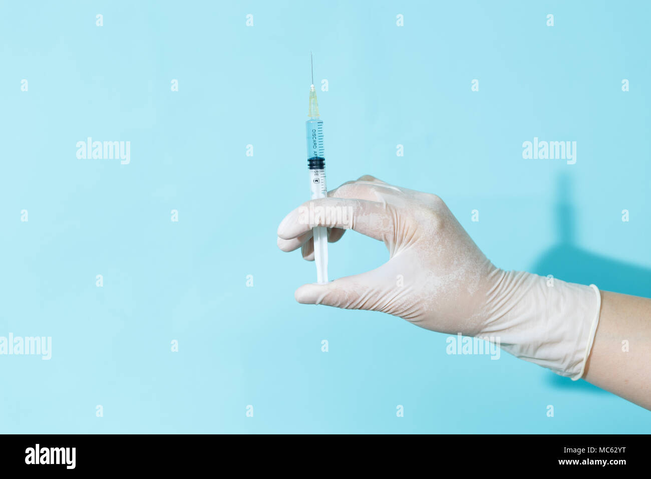 Un médecin gantée est titulaire d'une seringue sur un fond bleu Banque D'Images
