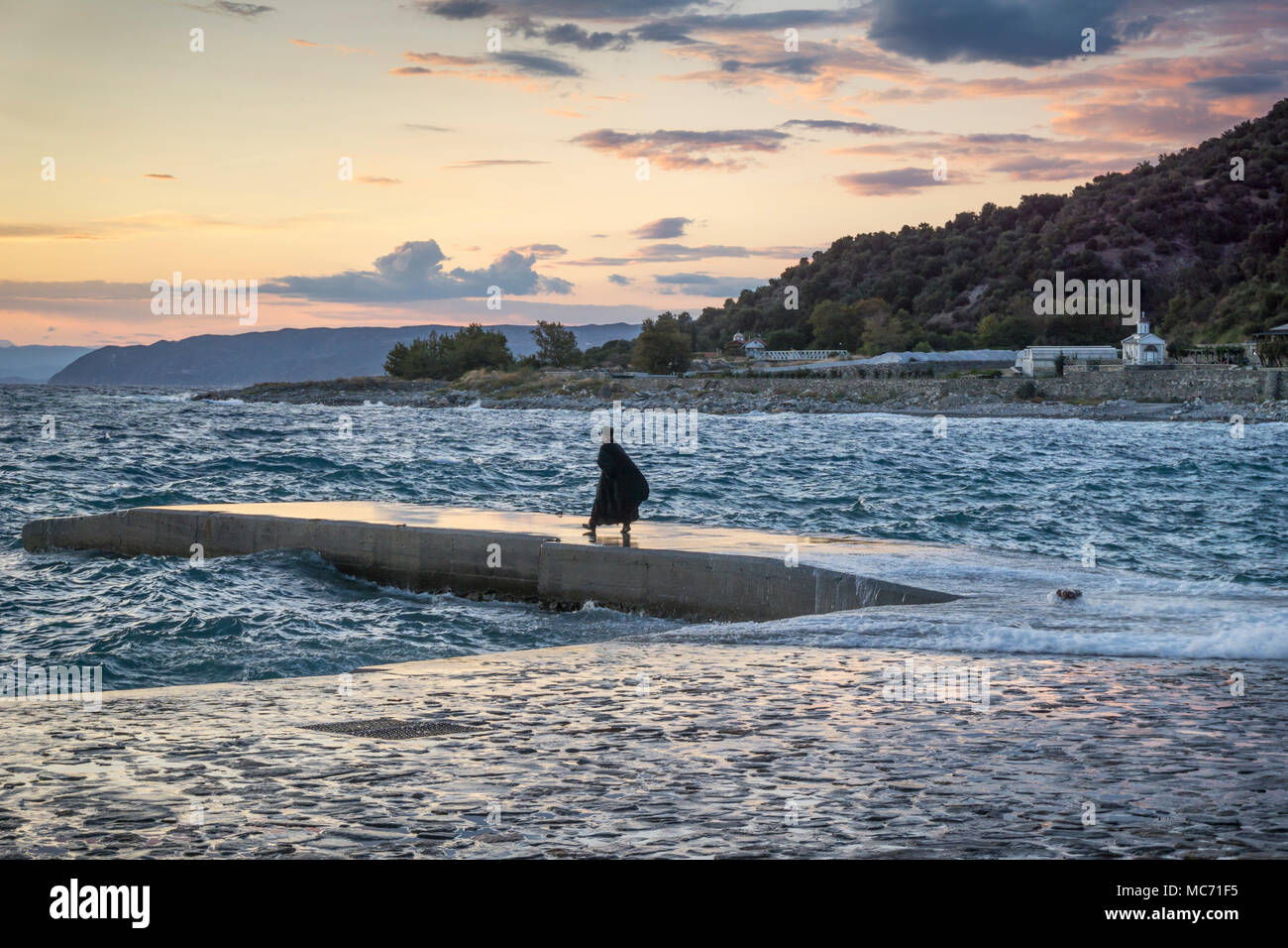 Un moine de Saint Panteleimon monastère sur le mont Athos watches le coucher de soleil depuis le quai. Péninsule Athos, Chalcidique, Macédoine, la Grèce du Nord. Banque D'Images