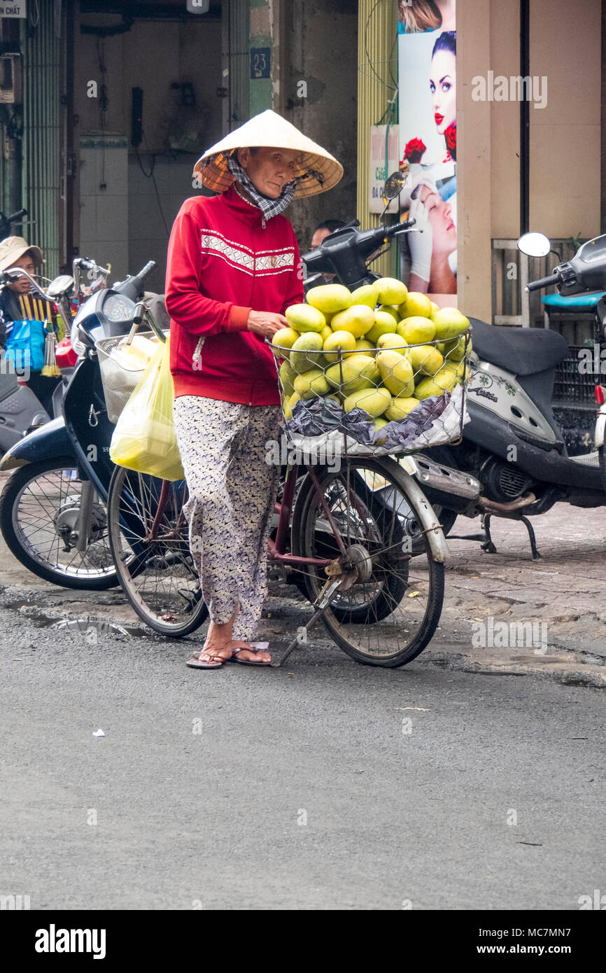 Une femme portant un chapeau conique de vendre un panier plein de mangues de son vélo dans une rue à Ho Chi Minh City, Vietnam. Banque D'Images