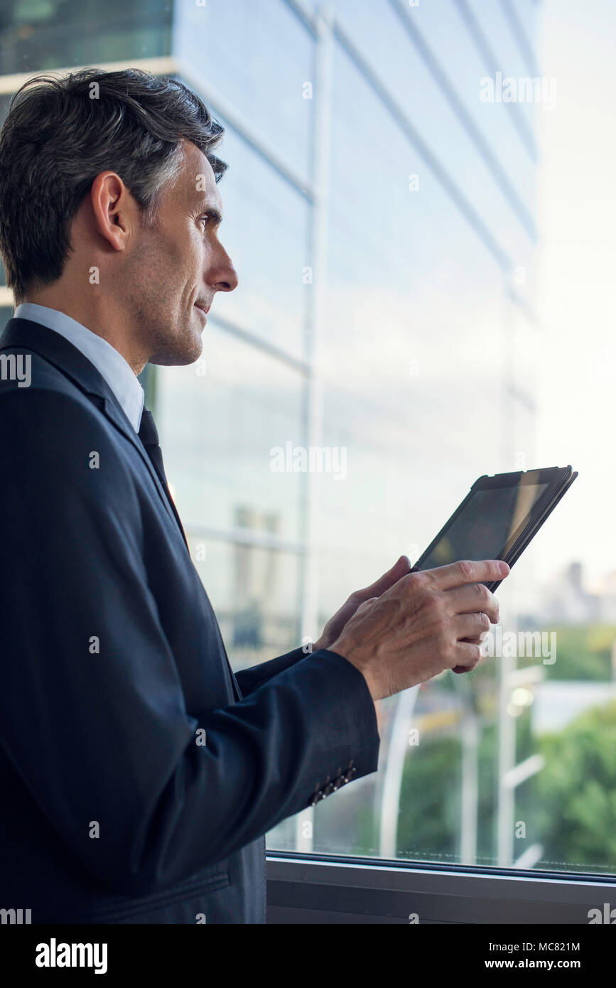 Man with digital tablet par fenêtre dans immeuble Banque D'Images