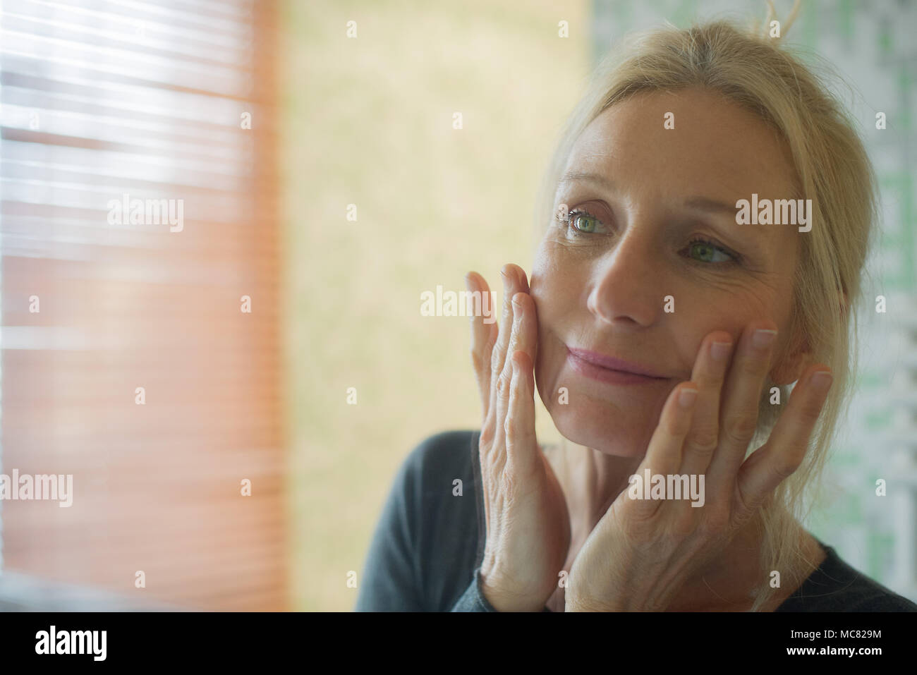 Femme mature à son reflet dans le miroir avec les mains sur les joues Banque D'Images
