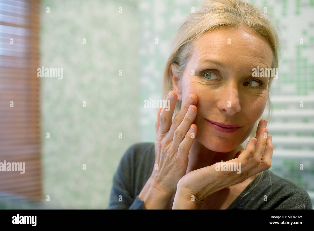 Femme mature à la recherche à la réflexion dans le miroir avec la main sur la joue Banque D'Images
