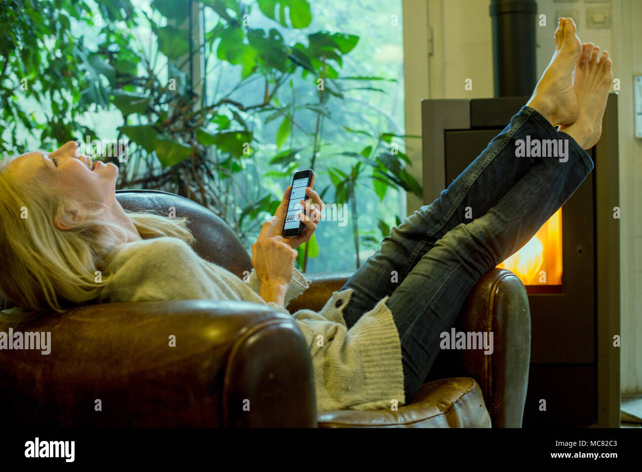Femme mature de rire tout en vous relaxant à la maison avec le smartphone Banque D'Images