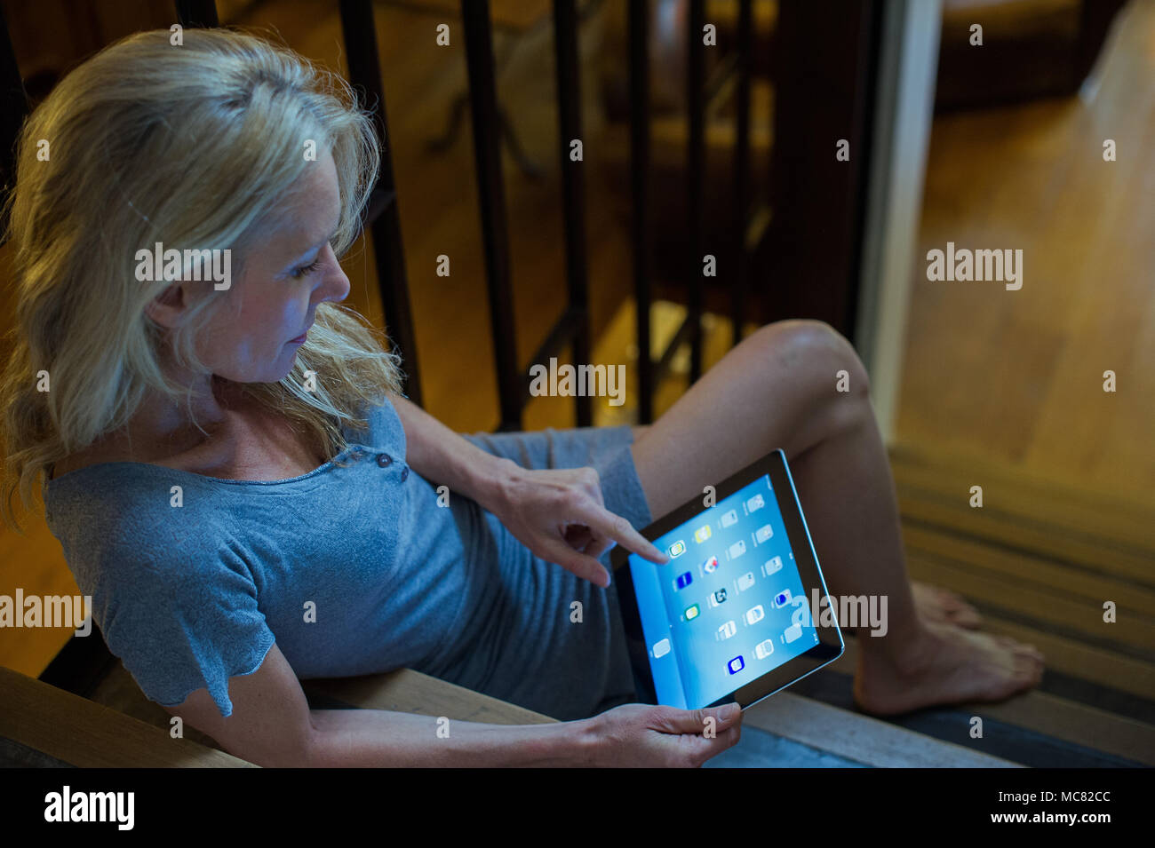 Mature Woman sitting on stairs at home, using digital tablet Banque D'Images