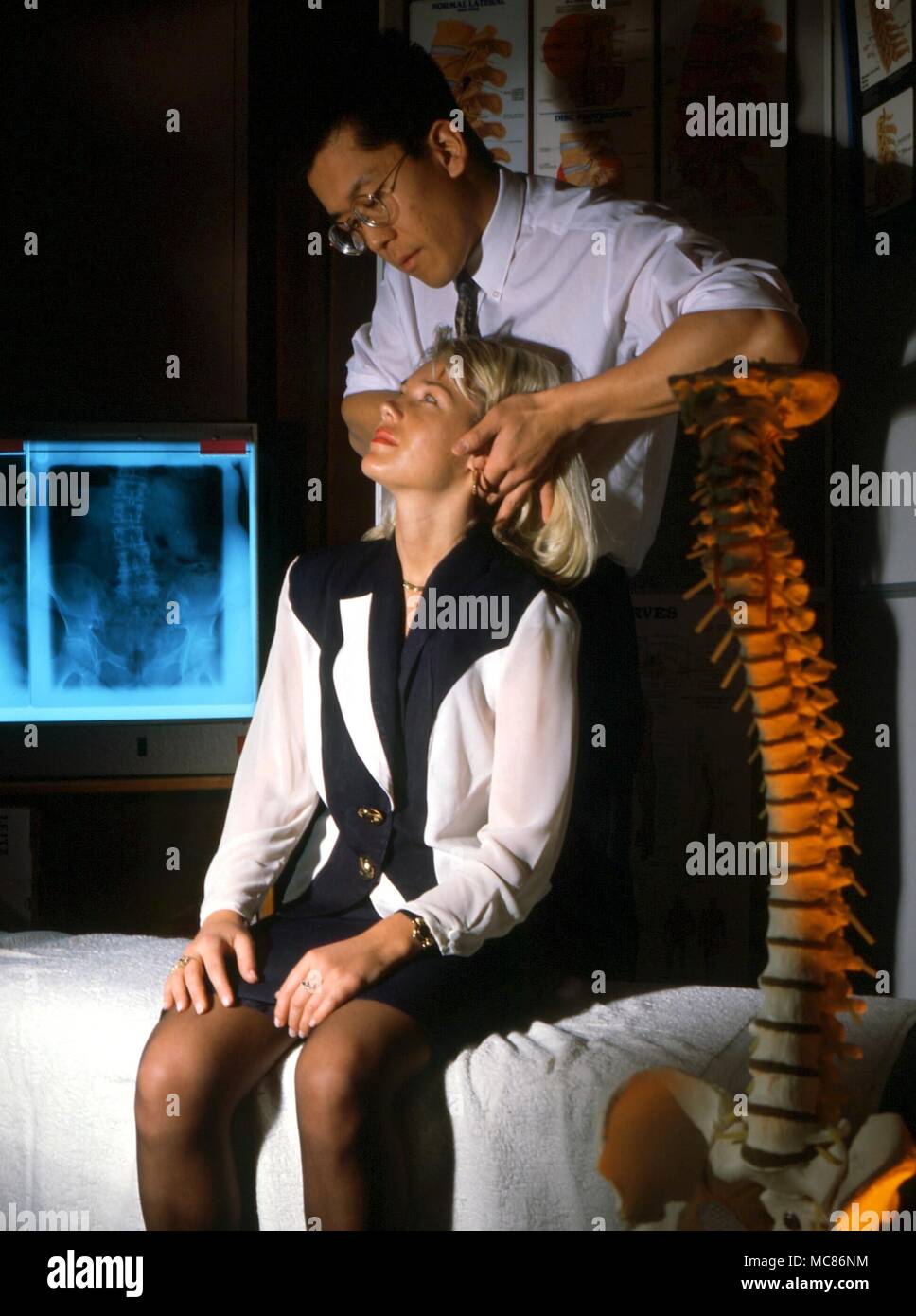 Le chiropraticien CARNET ROSE, Paul Cheung, démontrant son art durng une exposition. Les rayons X de la colonne vertébrale, ainsi que les maquettes du système squelettique de la colonne vertébrale, sont importants dans le diagnostic et dans le cadre des explications Banque D'Images