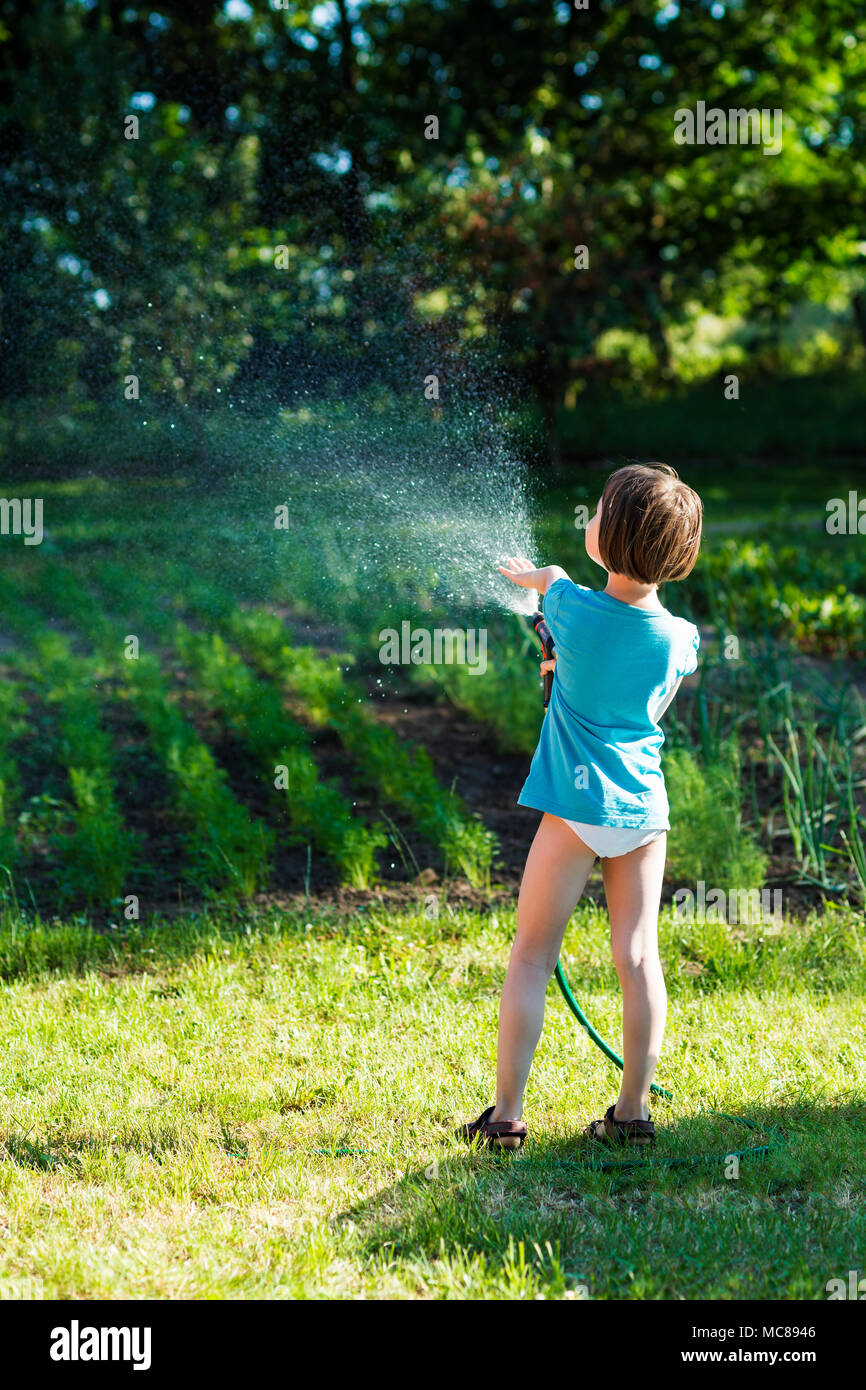 Petite fille enfant arroser les légumes dans un petit jardin. Banque D'Images