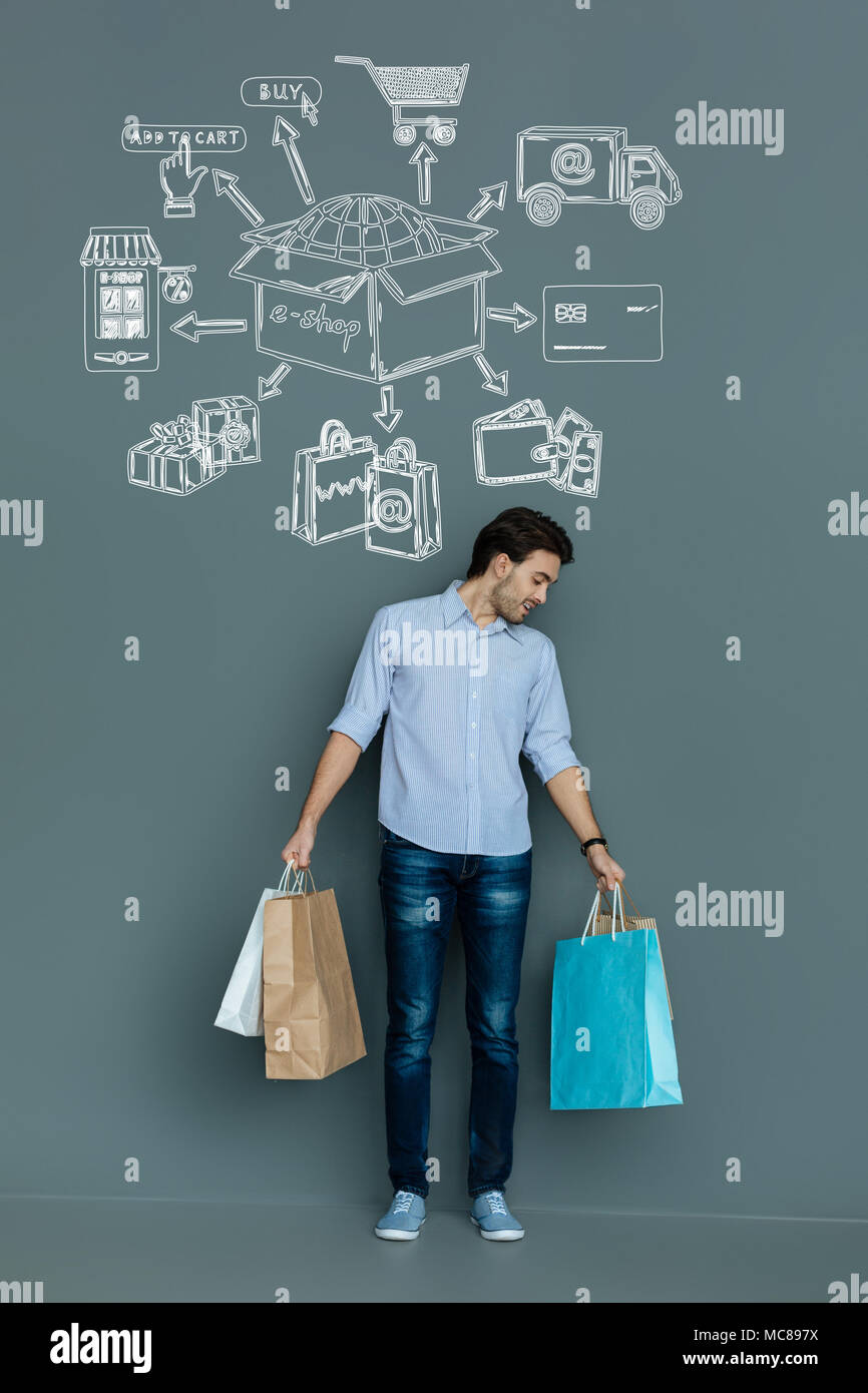 Cheerful man se sentir satisfait de son achat tout en maintenant les sacs en papier Banque D'Images