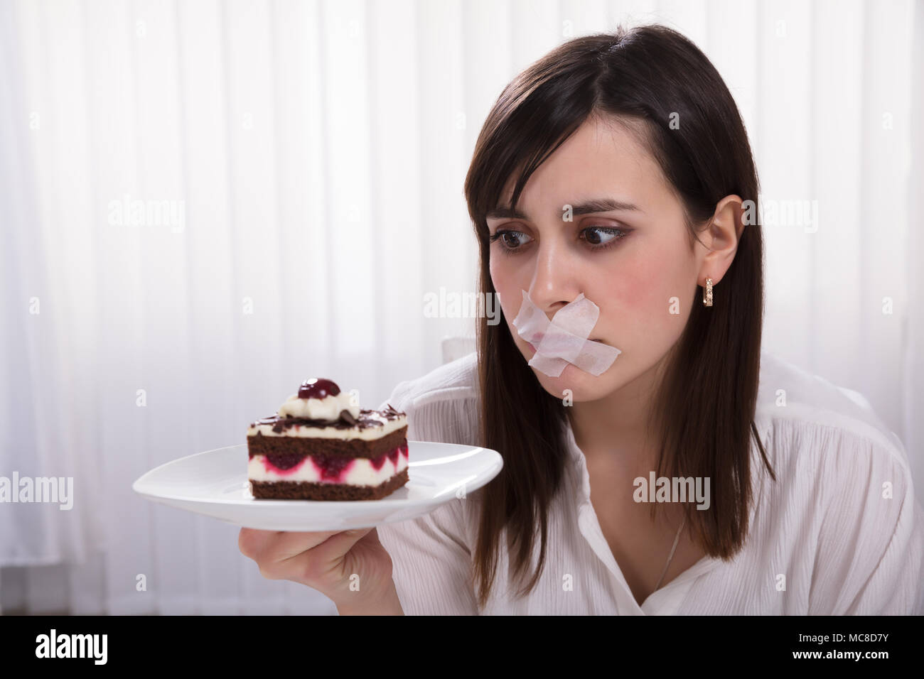 Jeune femme avec du ruban gommé sur la bouche Holding tranche de gâteau sur la plaque Banque D'Images