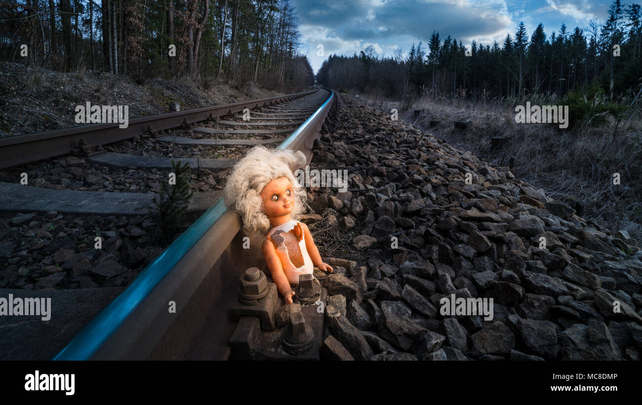 La voie du train avec de vieux doll éclairées par la lumière du mystère. Broken toy de l'enfant abandonné rusty rail dans la forêt. Idée du sort, apocalypse, science-fiction, de guerre ou d'abus. Banque D'Images