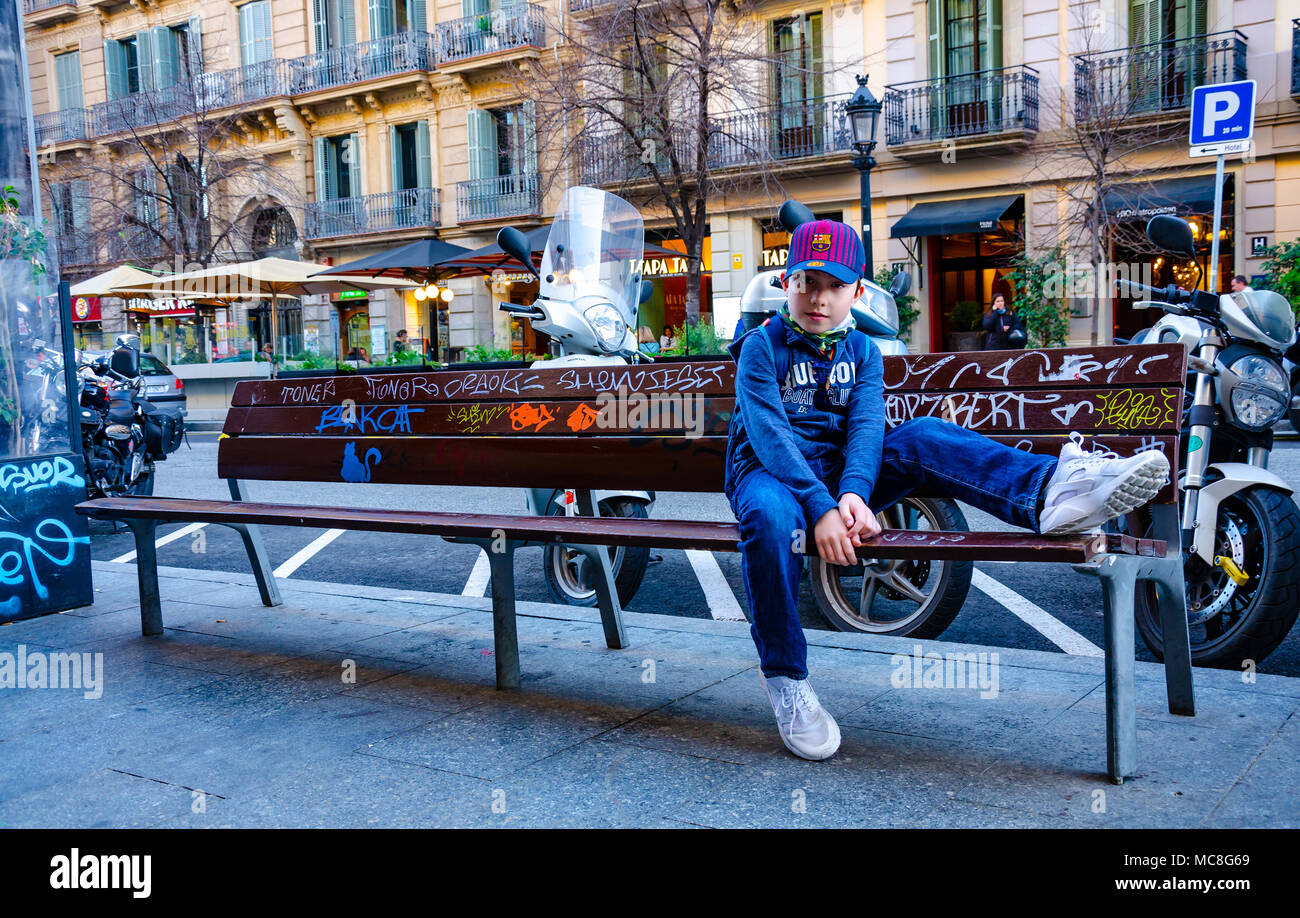 Un garçon est assis sur un banc à Barcelone qui est couvert de graffitis. Banque D'Images