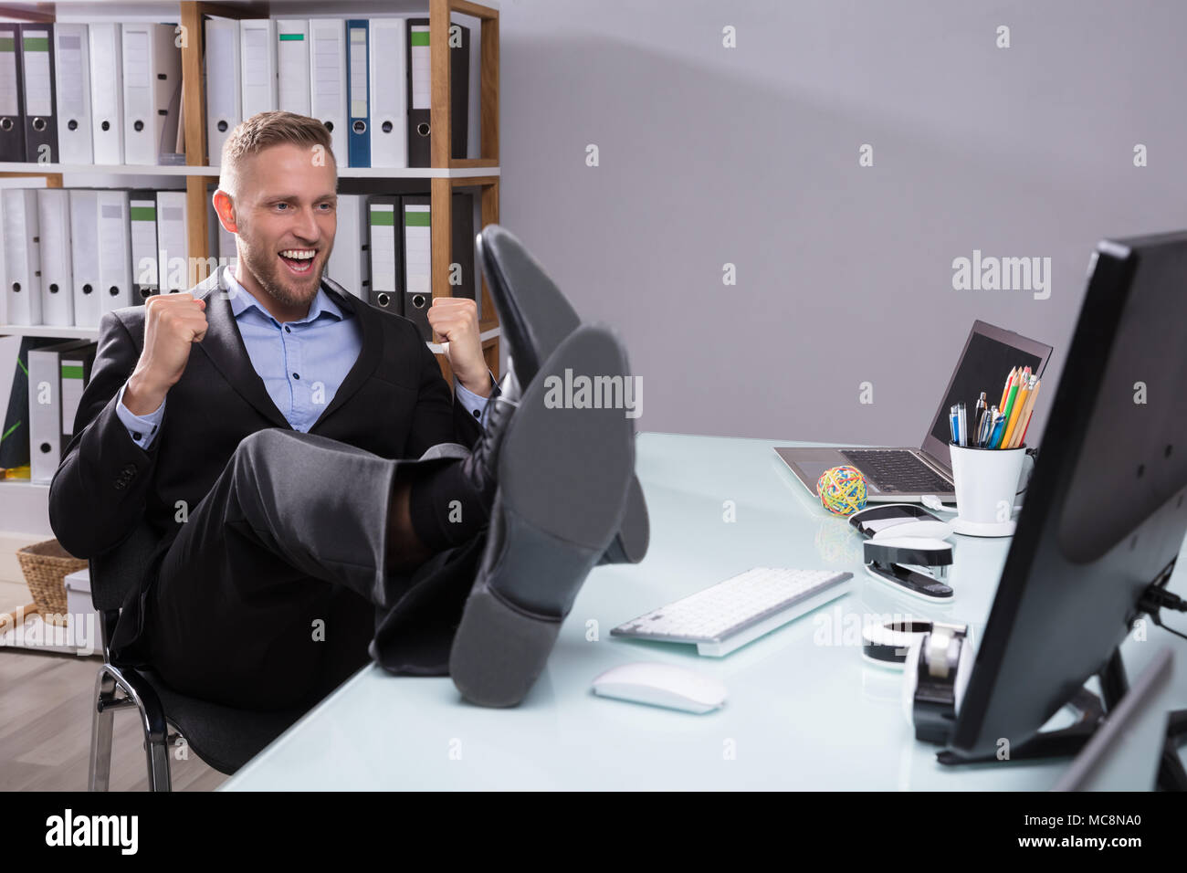 Excited Businessman Looking At Computer avec pieds sur Desk In Office Banque D'Images