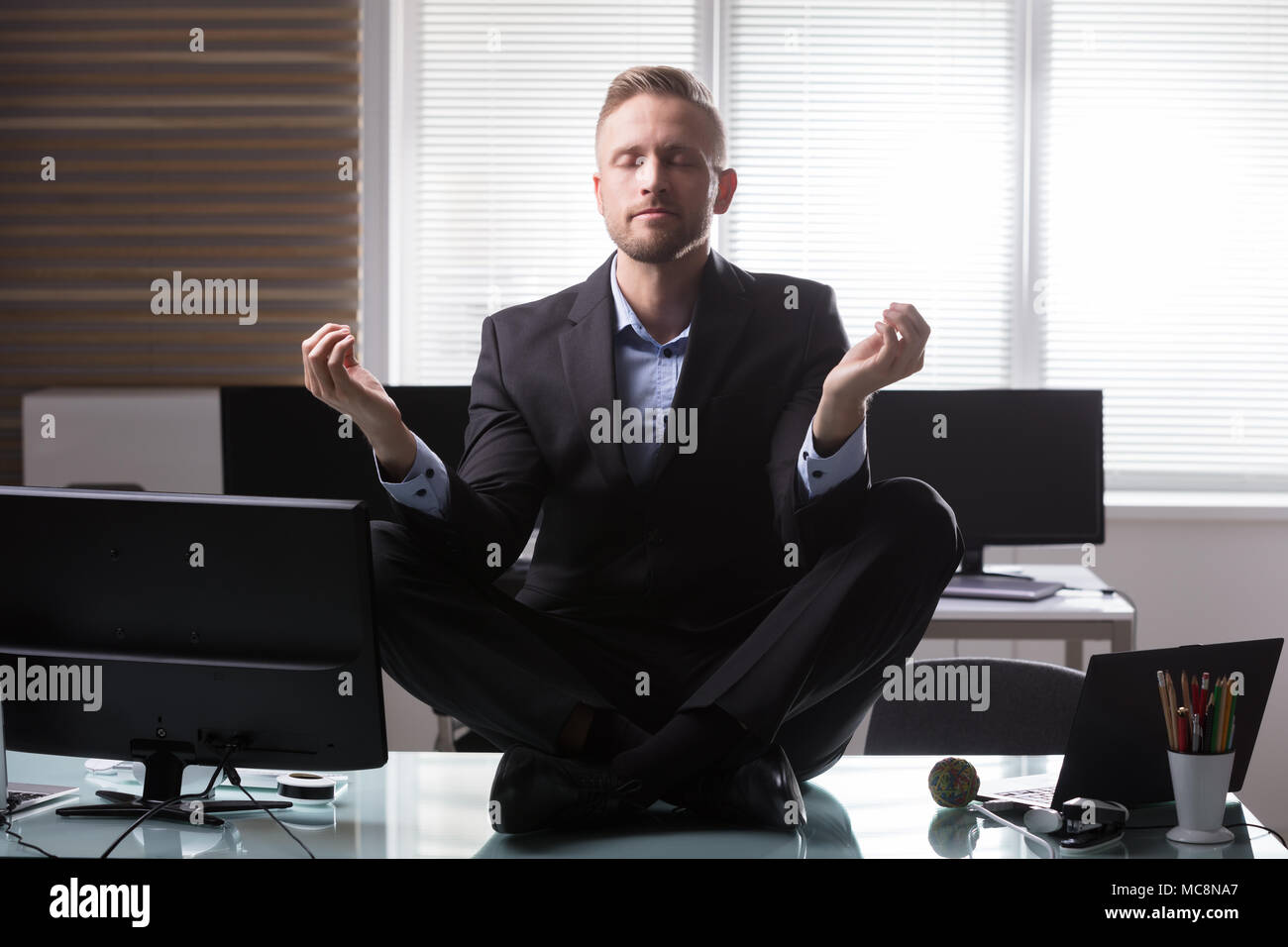 Young Businessman Sitting on Desk In Office Banque D'Images
