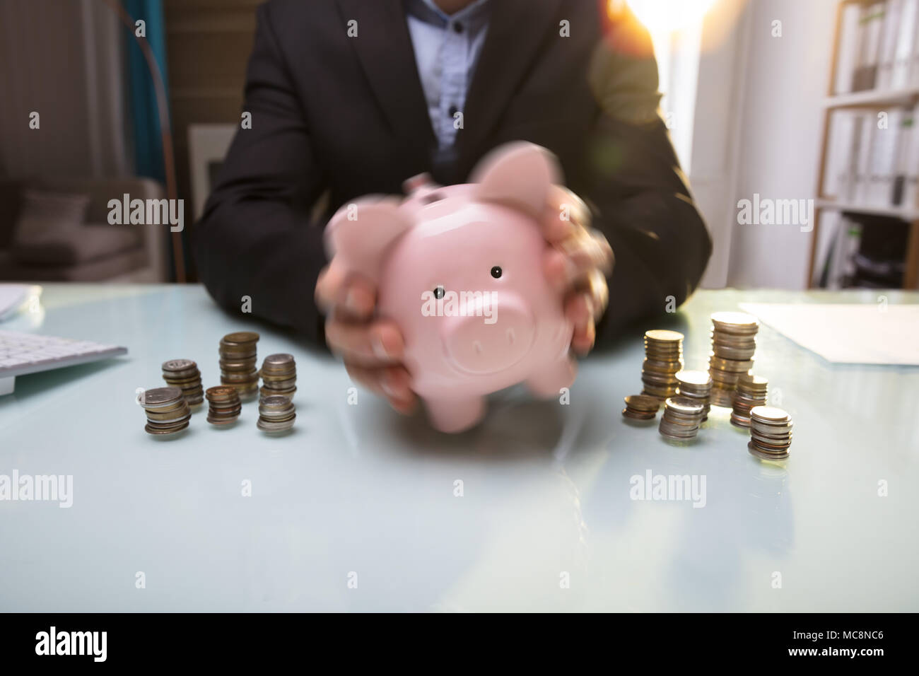 Close-up de l'homme d'affaires's Hand Shaking Tirelire près de pièces empilées Banque D'Images