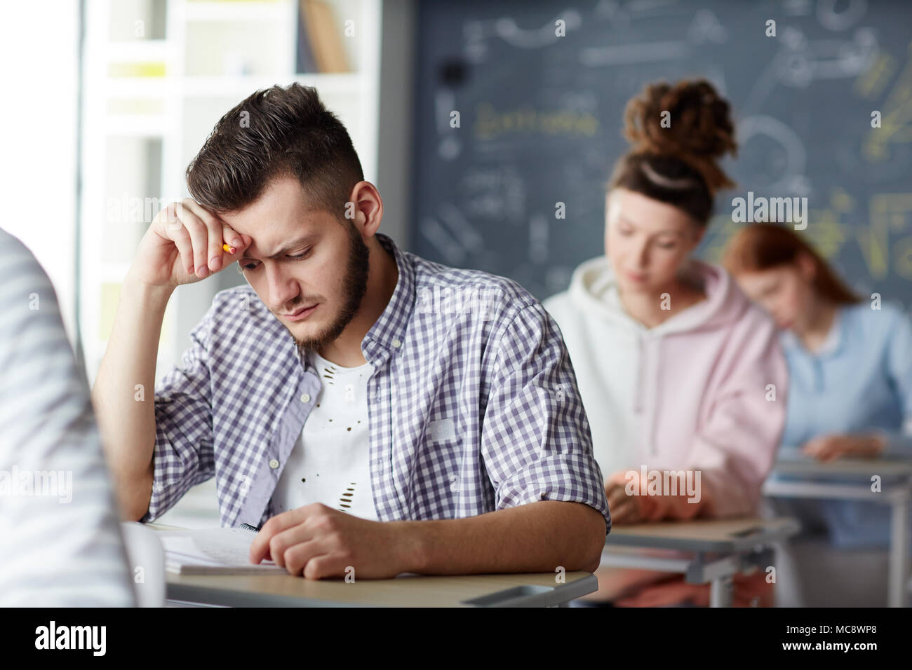 Pensive guy à à des questions sur papier test examen et d'essayer de se souvenir de la réponse à l'un d'eux Banque D'Images