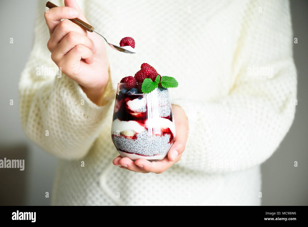 Girl in white sweater détient avec verre de lait chia dessert, framboises, bleuets, menthe. Petit-déjeuner sain concept. L'espace de copie, Close up Banque D'Images