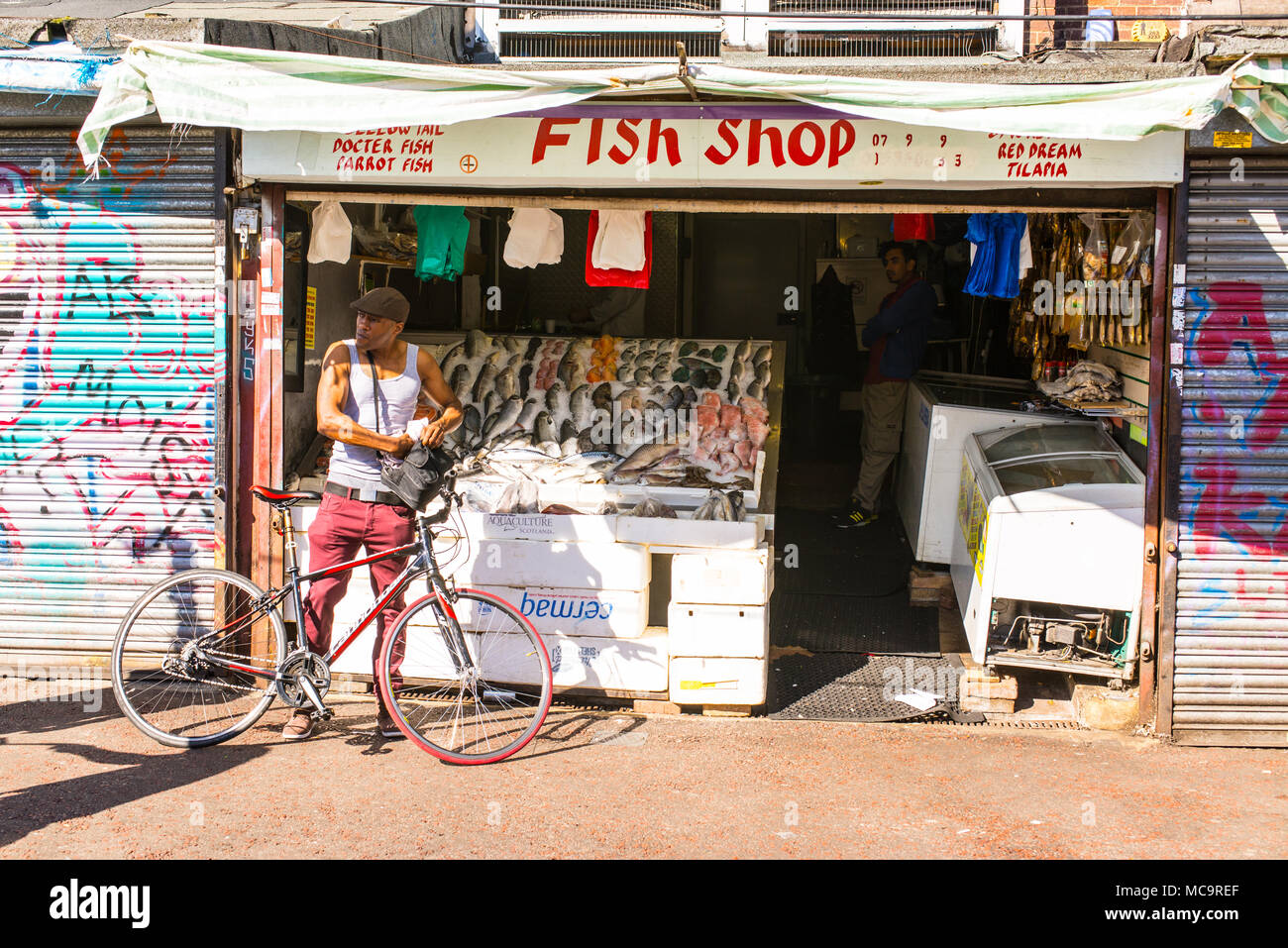 Petit poisson local indépendant shop poissonnier dans Ridley Road market avec le client sur l'arrêt de vélo en face d'elle dans le coeur de Dalston, East London, Banque D'Images