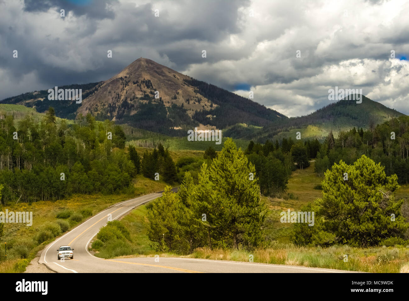 Vue d'une route entre les sommets des montagnes du Colorado, USA ; nuages orageux sur les sommets ; une voiture roulant Banque D'Images