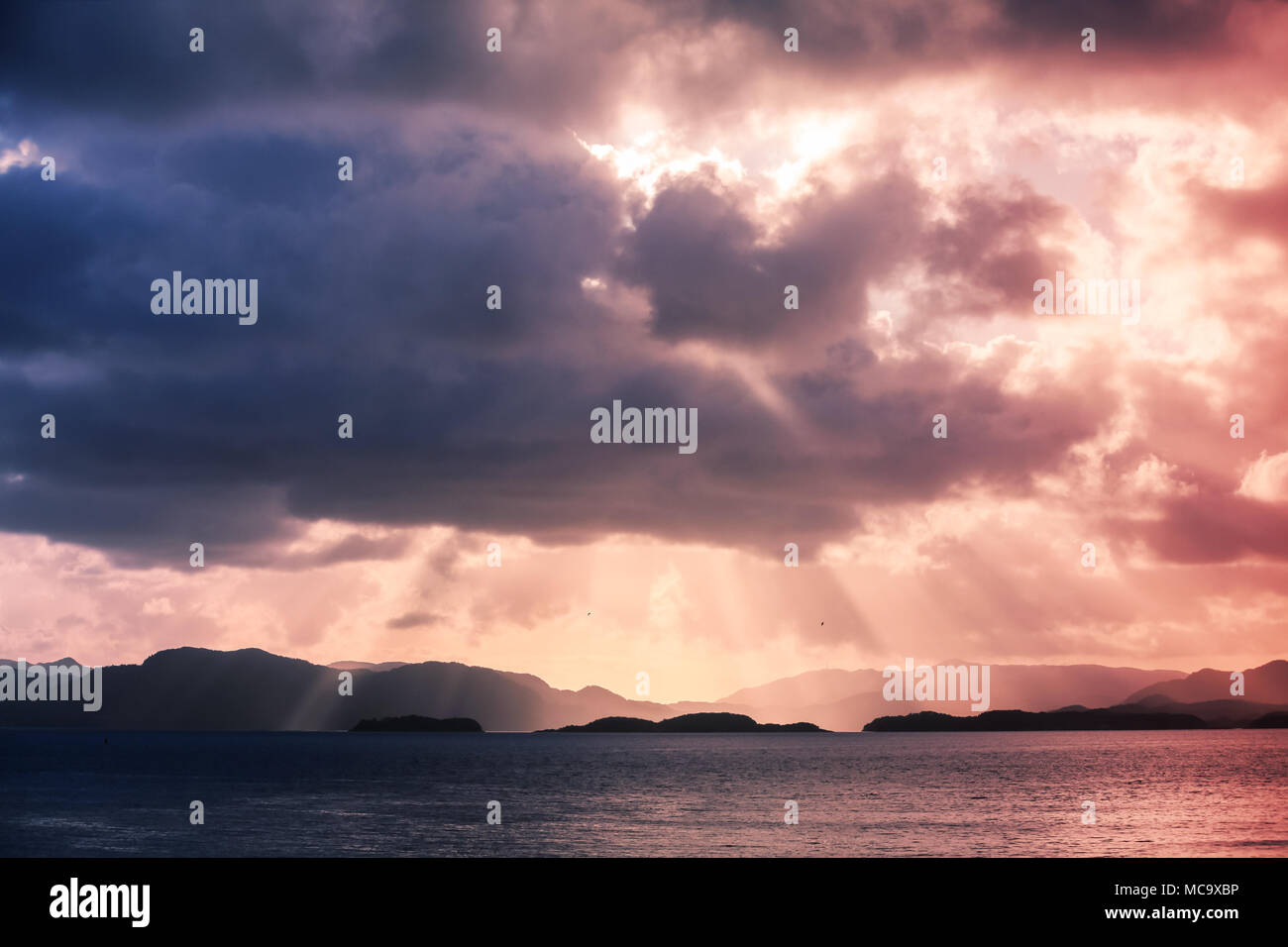 Paysage côtier norvégien avec vue sur la mer et les rayons de soleil colorés dans le ciel dramatique Banque D'Images