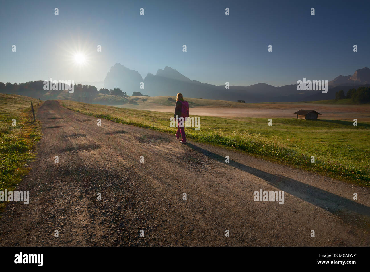 Jeune femme en randonnée sur la route de gravier vers les sommets des montagnes au lever du soleil. Le paysage ou l'Alpe di Siusi Alpe di Siusi - gamme de montagne Dolomites, Italie. Banque D'Images