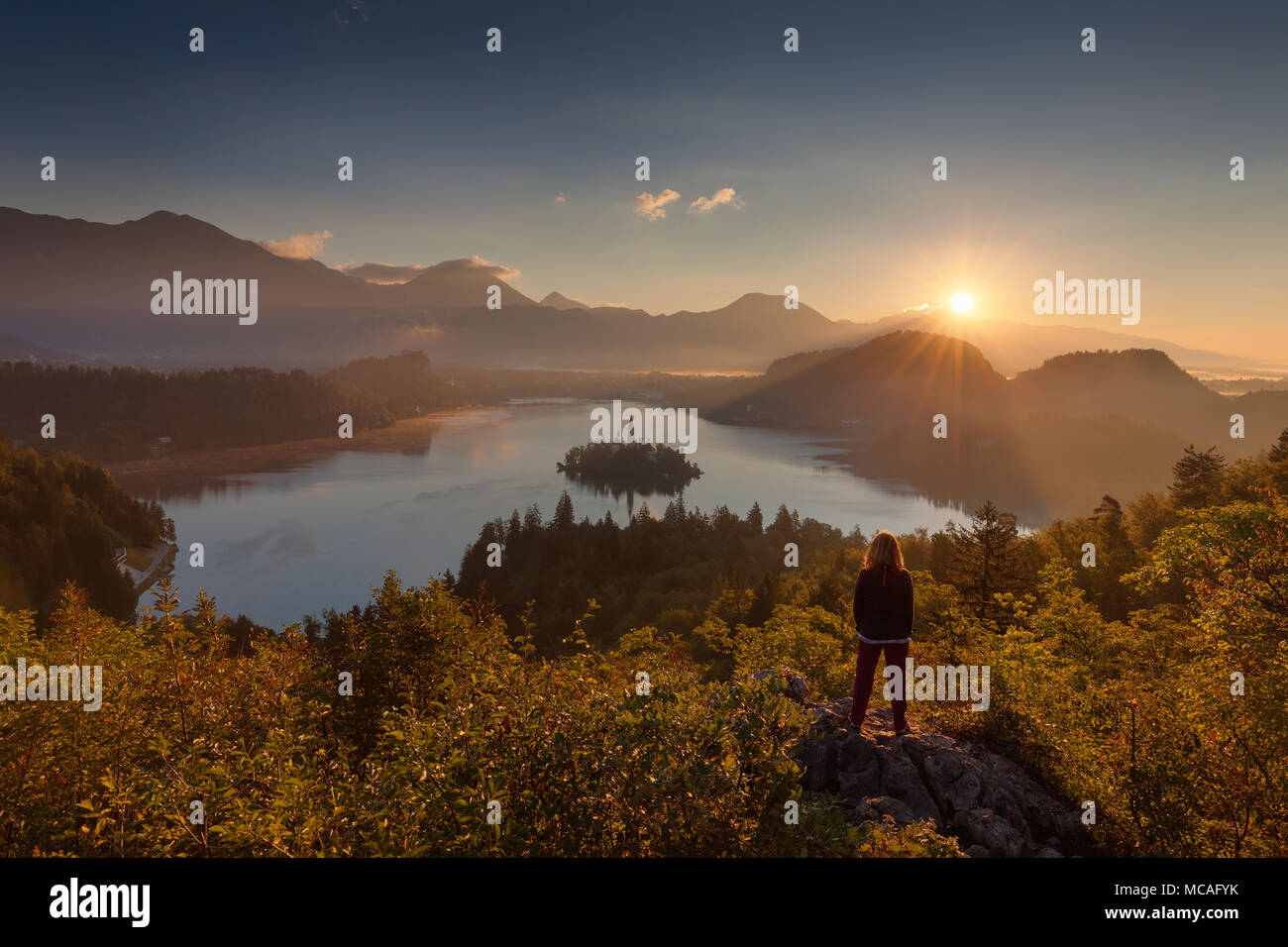 Lone woman standing on vue et regardant le soleil levant au-dessus du lac de Bled, en Slovénie. Concept de vie. Banque D'Images