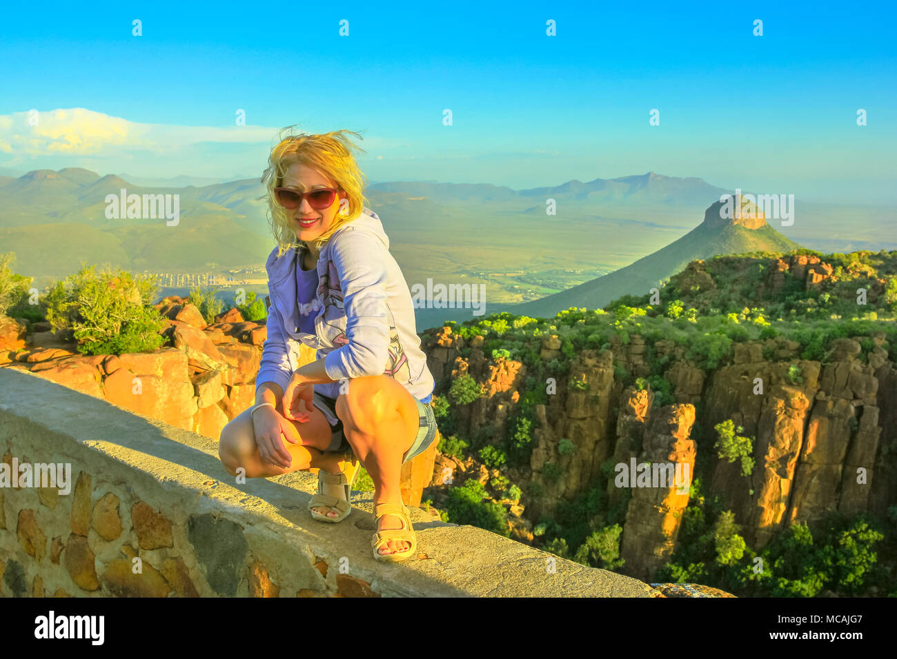 Happy tourist assis sur les rochers après une randonnée en vallée de la désolation, près de Graaff-Reinet, Afrique du Sud.Le coucher du soleil la lumière. Femme blonde profitant de vues aériennes de Camdeboo Parc National, Karoo, Liège Banque D'Images