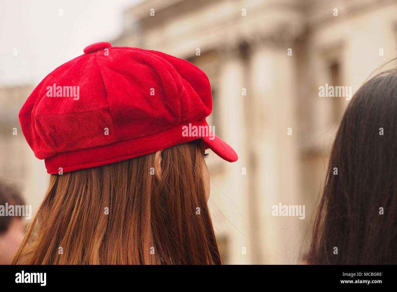 La tête d'une jeune femme aux longs cheveux bruns et portant un chapeau rouge à Trafalgar Square, Londres Banque D'Images