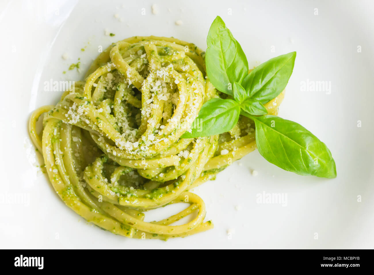 Les pâtes spaghetti avec sauce verte pesto original à Gênes (Genova) Italie sur plaque blanche fond, pâtes avec pesto de basilic herbes arrière-plan. Banque D'Images