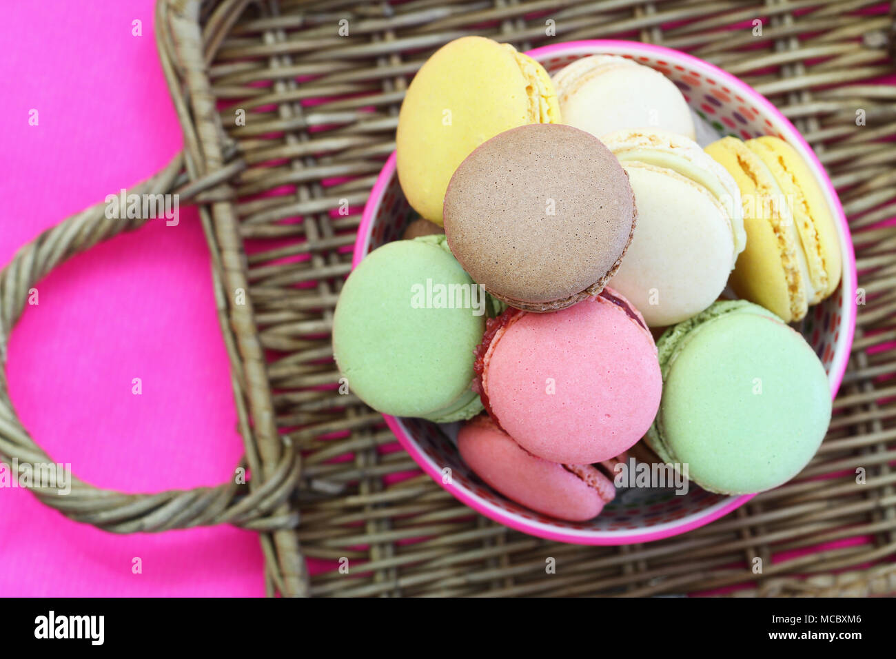 Sélection de macarons colorés dans un bol sur la surface en osier Banque D'Images